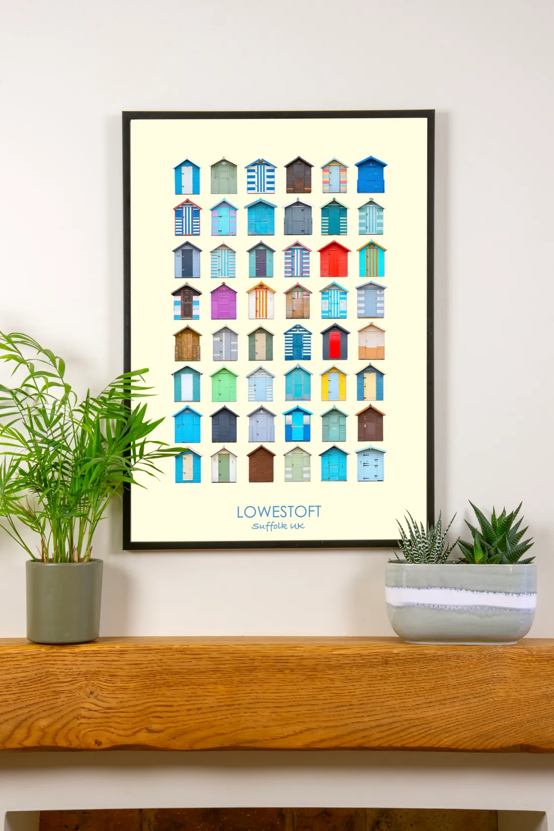The Lowestoft print in a slim black frame on a cream wall above an oak mantel shelf, between a palm and a succulent